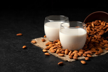 almond milk without sugar and lactose in glass with sprinkled nuts, vegetarian milk drink on a black table, copy space
