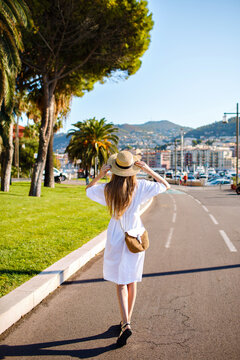 Outdoor travel picture of stylish young woman wearing elegant dress hat and straw back walking alone at amazing France small city, enjoying her trip, summertime vacations.