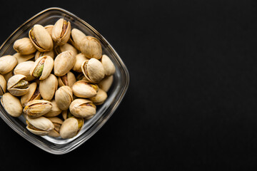 Pistachios in a small plate on a black table. Pistachio is a healthy vegetarian protein nutritious food. Natural nuts snacks.