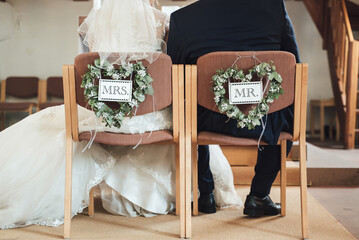 Rear view of couple sitting on chairs decorated with flower hearts and tables Mr. and Mrs. Bride and groom at wedding ceremony. Wadding day concept.
