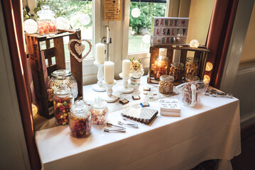 Salty and candy bar of several kinds of salty snacks and colorful candies in glass jars decorated with candles on white clothed table.Wedding or party