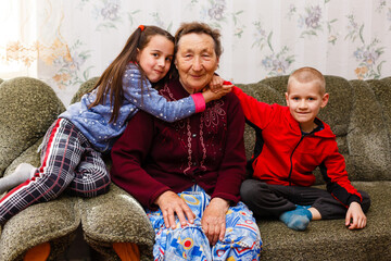 Closeup portrait of happy great-grandmother with great-grandchildren on the sofa at home