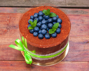 Chocolate honey cake with grated walnuts and prunes, blueberries, and mint decorate the top of the cake. On a wooden table