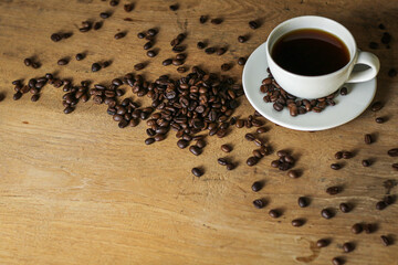 White coffee cup and coffee beans on wooden table with copyspace for text. Selective focus.