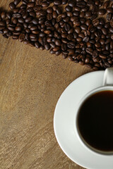 White coffee cup and coffee beans on wooden table with copyspace for text. Selective focus.