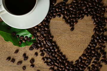 White coffee cup and coffee beans on wooden table with heart copyspace for text. Selective focus.