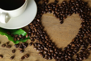 Naklejka premium White coffee cup and coffee beans on wooden table with heart copyspace for text. Selective focus.