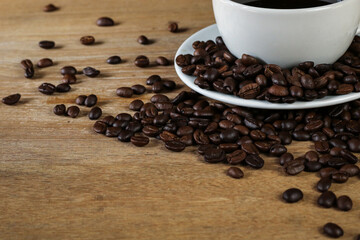 White coffee cup and coffee beans on wooden table with copyspace for text. Selective focus.