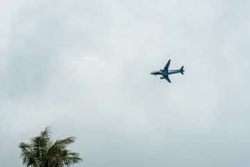 Plane flying in a cloudy sky and preparing to land on a tropical island.