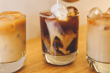 coffee being poured into milk glass with ice cubes at wood table