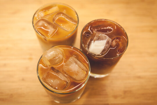 three glasses of iced coffee being at wood table