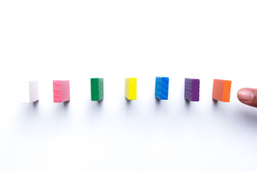 A picture of hand going to push colourful dominoes.