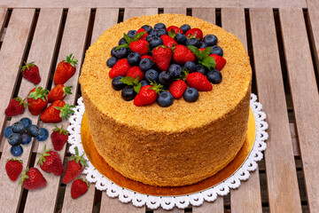 A large 3 kg honey cake with walnuts, strawberries, blueberries, and mint decorate the top of the cake. On a wooden table