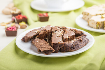 traditional arabic sweets sesame halva with chocolate and pistachio and a cup of coffee on green textile background. side view, selective focus.