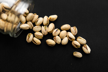 Pistachio scattered on the black table from a jar. Walnut is a healthy vegetarian protein nutritious food.