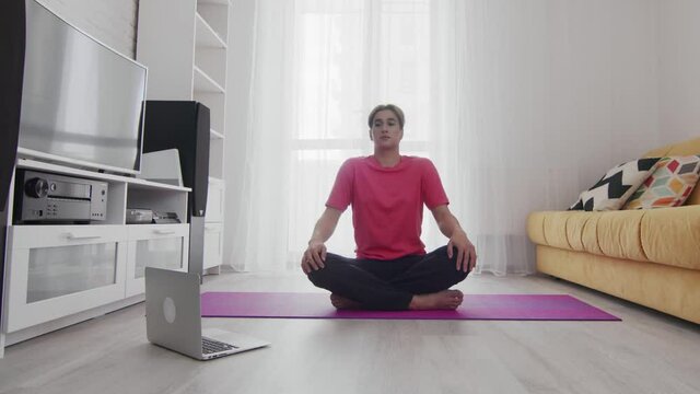 Young Transgender Homosexual Man With Makeup Rotates Sholders To Warm Up Before Exercise And Looks At The Laptop Online Instructiong At Home