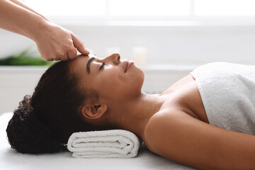 Relaxed black girl lying at spa, having head massage