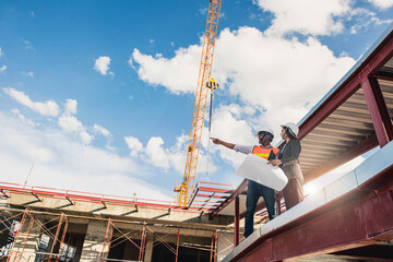 Naklejka premium Engineer in hardhat and orange jacket posing on building site. civil engineer or architect with hardhat on construction site checking schedule on plan.