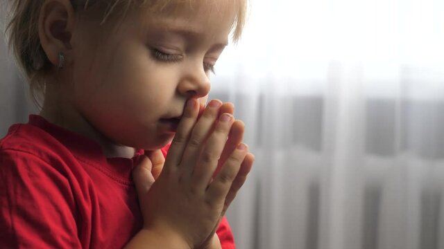 lifestyle little daughter girl makes a wish prayers bedtime religion concept . prayer child indoors praying by bed in front of window