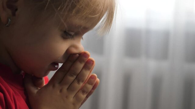 little daughter girl makes a wish prayers bedtime religion concept . prayer lifestyle child indoors praying by bed front of window