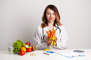 Young dietitian doctor at the consulting room at the table with fresh vegetables and fruits, working on a diet plan