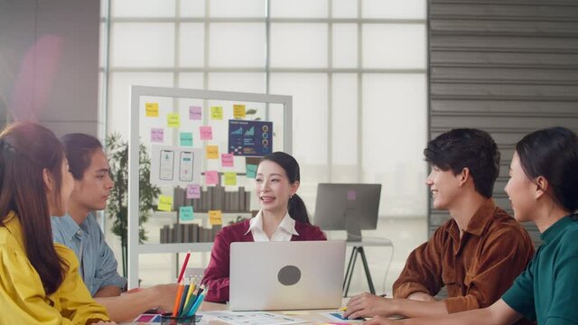 Multiracial group of young creative people in smart casual wear discussing business shaking hands together and smiling while standing in modern office. Partner cooperation, coworker teamwork concept.