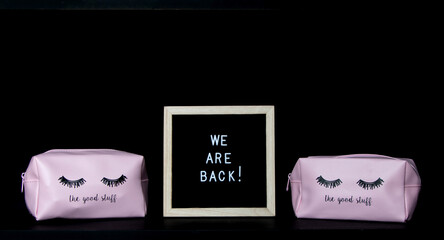 we're back!  phrase enclosed in a wooden frame in the middle of two pink wallets with a black background