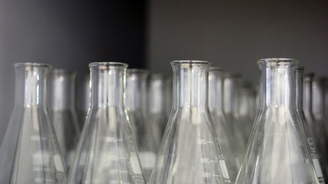 Transparent Erlenmeyer flasks or conical flasks on shelf in science laboratory, use for measuring solvent or solution, titrations of chemistry experiment for analysis sample. Selective focus on flask.