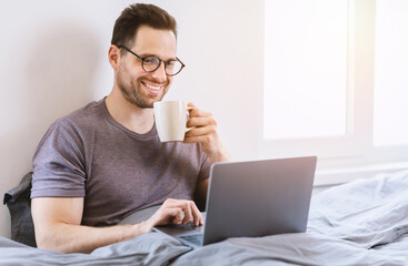 Man Using Laptop Browsing Internet Sitting In Bed At Home