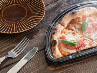 テーブル上のナイフとフォーク、そしてテイクアウト容器に入ったピザ。