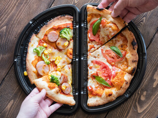 ソーセージピザとトマトピザのハーフアンドハーフを取る男性と女性の手。