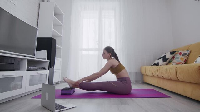 Young beautiful woman is doing stretching exercises on violet mat at home