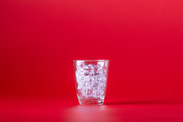 Glass with ice on a red background.