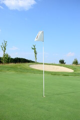 Fototapeta premium golf flag on green grass agains blue sky