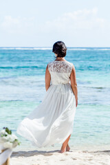 Bride back view in a white wedding dress walking on the sandy caribbean beach landscape on  sunny day in Dominican republic 