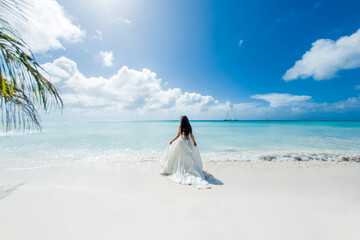 Bride back view in a white wedding dress walking on the sandy caribbean beach landscape on  sunny...