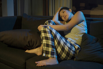 Obraz premium Asian girl suffering depression - sad and depressed Chinese woman crying on darkness in pain feeling worried and helpless sitting at living room sofa couch overwhelmed