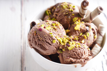 Chocolate ice cream balls with pistachio and cookies in a white bowl