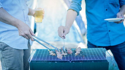 Two men pinging the barbecue on the stove and one hand holding a glass of beer.