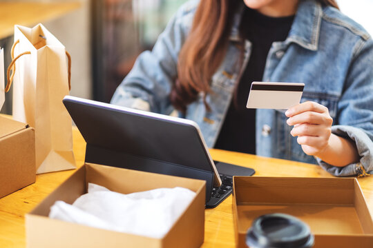 Closeup image of a young woman using tablet pc and credit card for online shopping , opening shopping bags and postal parcel box on the table