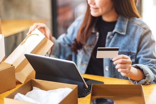 Closeup image of a young woman using tablet pc and credit card for online shopping , opening shopping bags and postal parcel box on the table