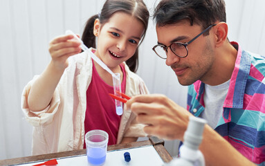 Little girl and her father doing science experiments in the laboratory. Dad and daughter study chemistry lesson with microscope and mixing liquids in the flasks for experiment. Homeschooling concept.