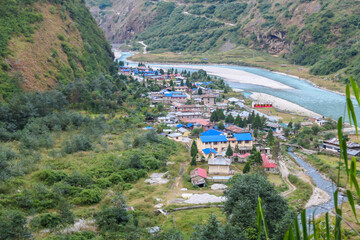 Fototapeta na wymiar Top down drone capture of turquoise river flowing at the bottom of Himalayan valley, surrounding small village Tal, Nepal. There is Annapurna Circuit Trek going along the valley. High mountain chains
