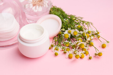 Cosmetic cream with chamomile flowers on color background