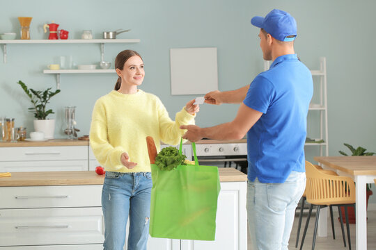 Young Woman Receiving Fresh Products And Business Card From Deliveryman At Home