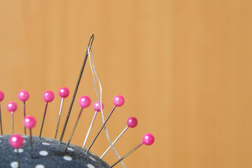 Needle with white thread and pink pins on pincushion for handmade sewing cloth with brown wood background close-up.