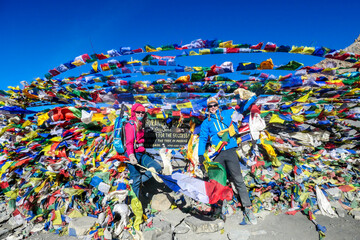 A couple standing between prayer flags at the top of Thorung La Pass, Annapurna Circuit Trek,...