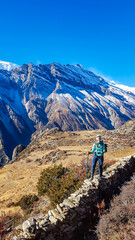 A woman standing at a stony wall while trekking Annapurna Circus, Himalayas, Nepal, with the view on Annapurna Chain. Dry and desolated landscape. High, snow capped mountain peaks. Happiness