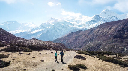 Fototapeta premium A couple trekking in the Manang Valley, Annapurna Circus Trek, Himalayas, Nepal, with the view on Annapurna Chain and Gangapurna. Dry and desolated landscape. High snow capped mountain peaks. Freedom