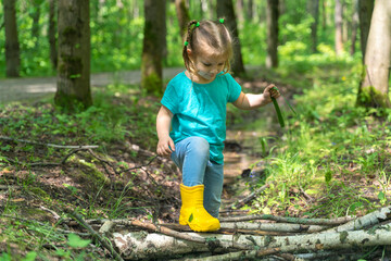 little girl walks through puddles in rubber boots in the forest